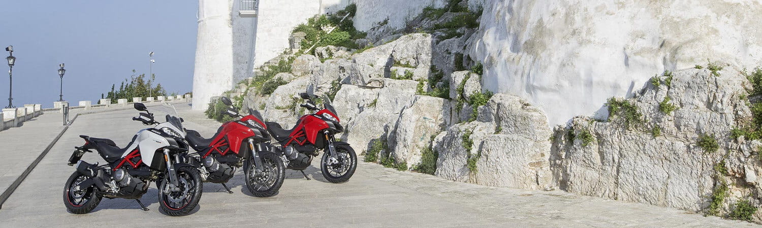 Three 2020 Ducati Multiestrada 950 motorcycles parked at a scenic visitor spot with white rock.